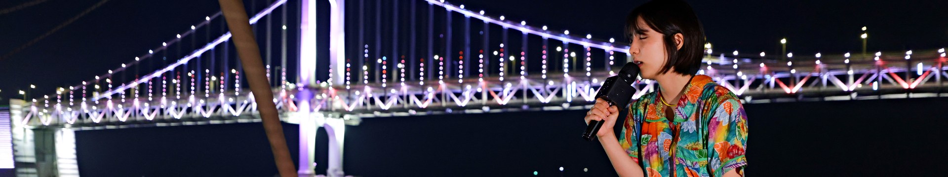 A busker singing at the bow of the yacht with Gwangan Bridge behind