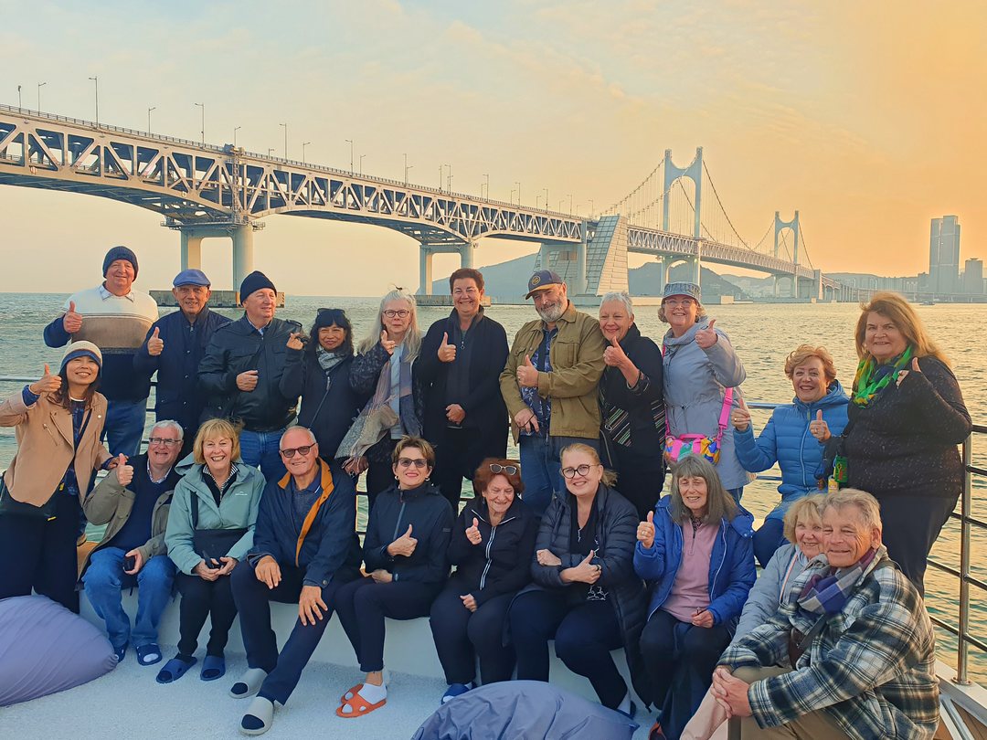 A group gathered on deck with Gwangan Bridge at sunset behind